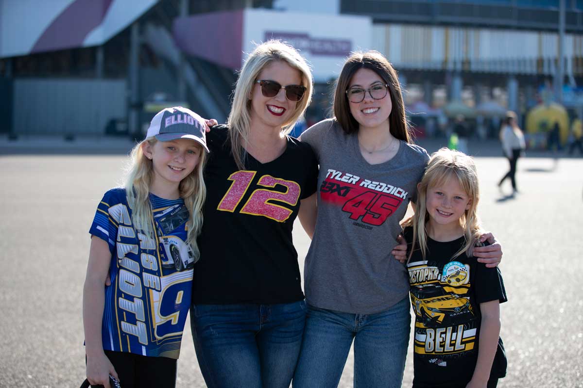 Two adults and two children smile for a photo in the fan area while wearing driver-themed apparel and hats.